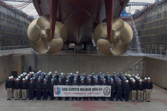 YOKOSUKA, Japan (Feb. 19, 2008) Sailors assigned to the Arleigh Burke-class guided-missile destroyer USS Curtis Wilbur (DDG 54) pose for a command photo under the ship's screws as the command wraps up a dry dock selective restricted availability. Curtis Wilbur is attached to Destroyer Squadron (DESRON) 15 and is permanently forward deployed to Yokosuka. U.S. Navy photo by Mass Communication Specialist 2nd Class Nardelito Gervacio