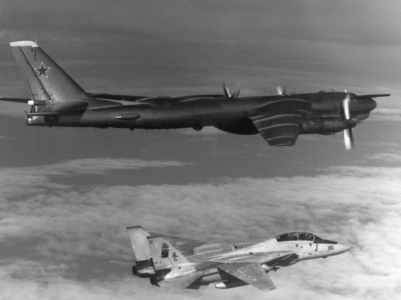 Air-to-air right side view of a Soviet TU-95 Bear-D aircraft with F-14A Tomcat aircraft from the fighter squadron (VA-11) below.