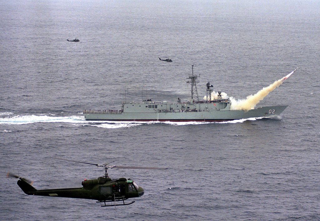 HMAS Canberra (F-02) lançando míssil Harpoon, enquanto helicópteros UH-1 Iroquois fazem a cobertura aérea do lançamento